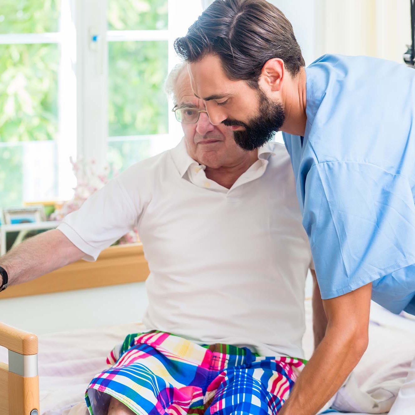 Elderly care nurse helping senior from wheel chair to bed