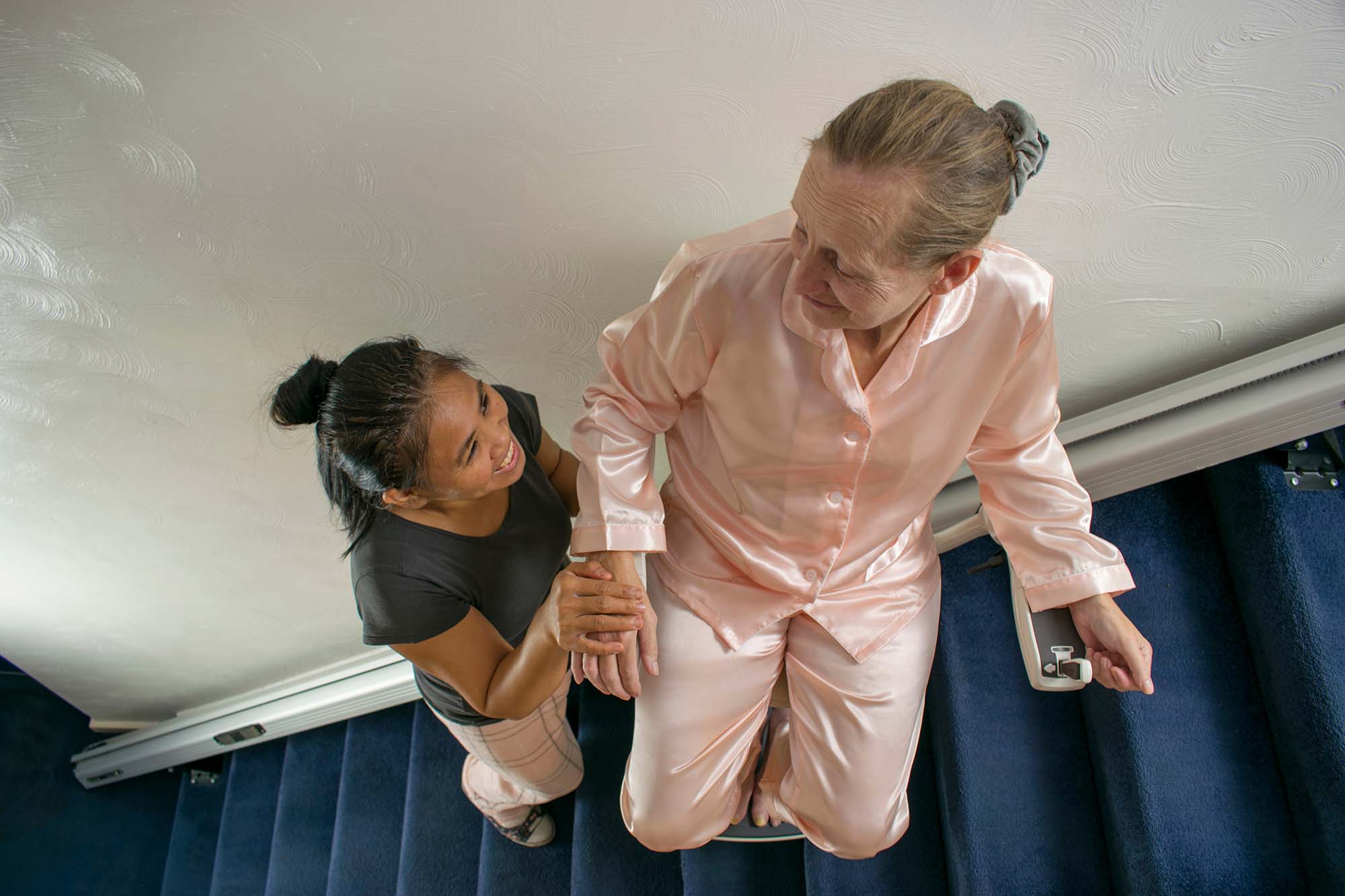 Carer helping elderly woman on a stairlift